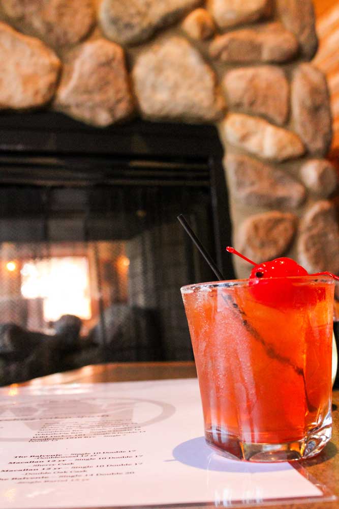 Cocktail garnished by cherries served in a warming rustic atmosphere at the cabin bar at Mackinaws Grill & Spirits in Green Bay WI.